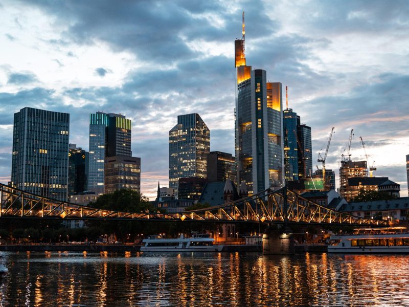 Cityscape of Frankfurt downtown at sunset, Germany. River Main with moored boats, skyscrapers with illumination on the background